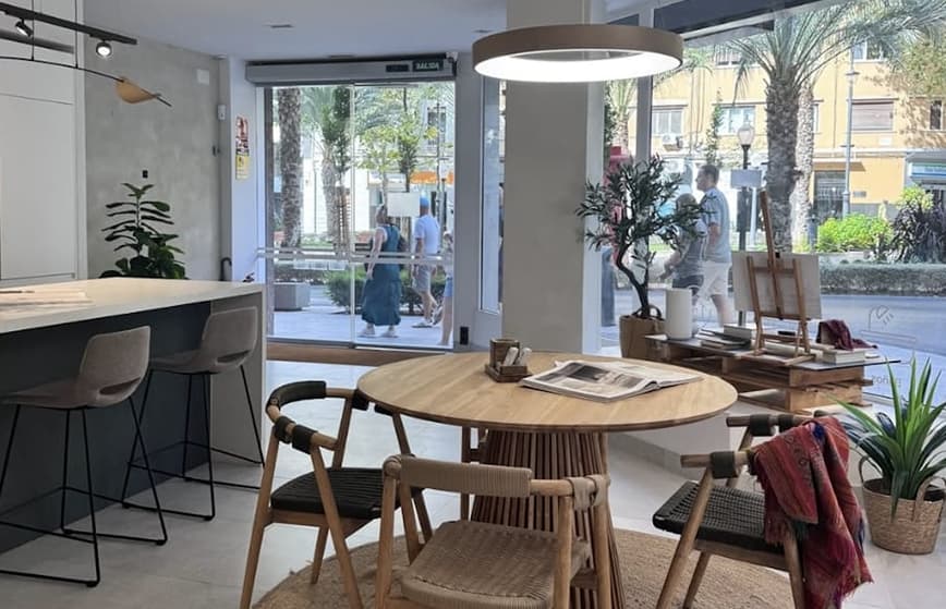 Espacio interior reformado con mesa redonda de madera y ventanales amplios en Alicante