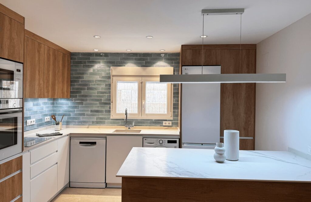 Cocina moderna con isla central y muebles de madera en la reforma de Casa Santa Pola